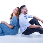 Happy couple sitting back to back in a studio, embracing togetherness and joy.