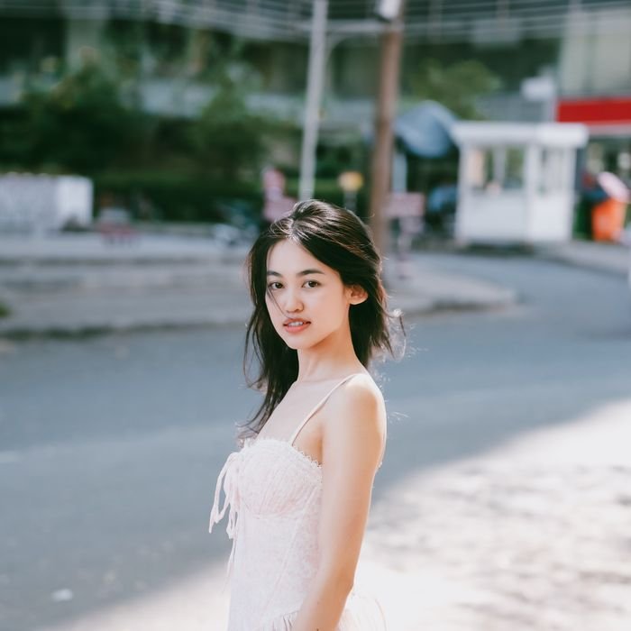 A young woman in a white dress smiles outdoors in Ho Chi Minh City, Vietnam.